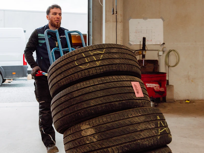 Technicien transportant plusieurs pneus dans l’atelier Bomerée-Pneus à Montigny-le-Tilleul.