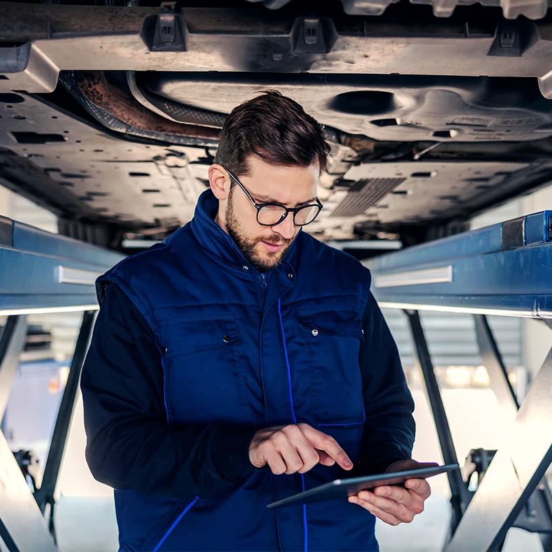 Technicien réalisant un diagnostic mécanique sous un véhicule sur pont élévateur chez Bomerée-Pneus.